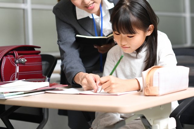 大人にノートを見てもらいながら学ぶ小学生のイメージ